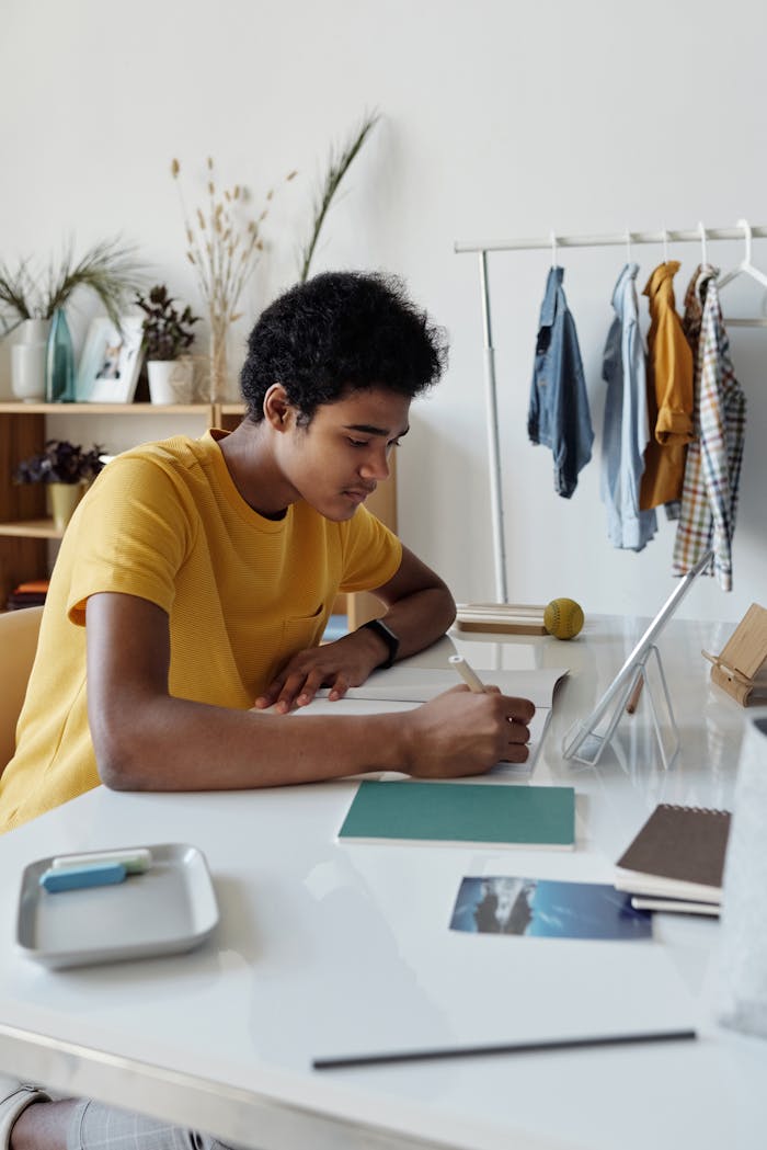 Focused African American teen studying indoors with a tablet and notebook at home.